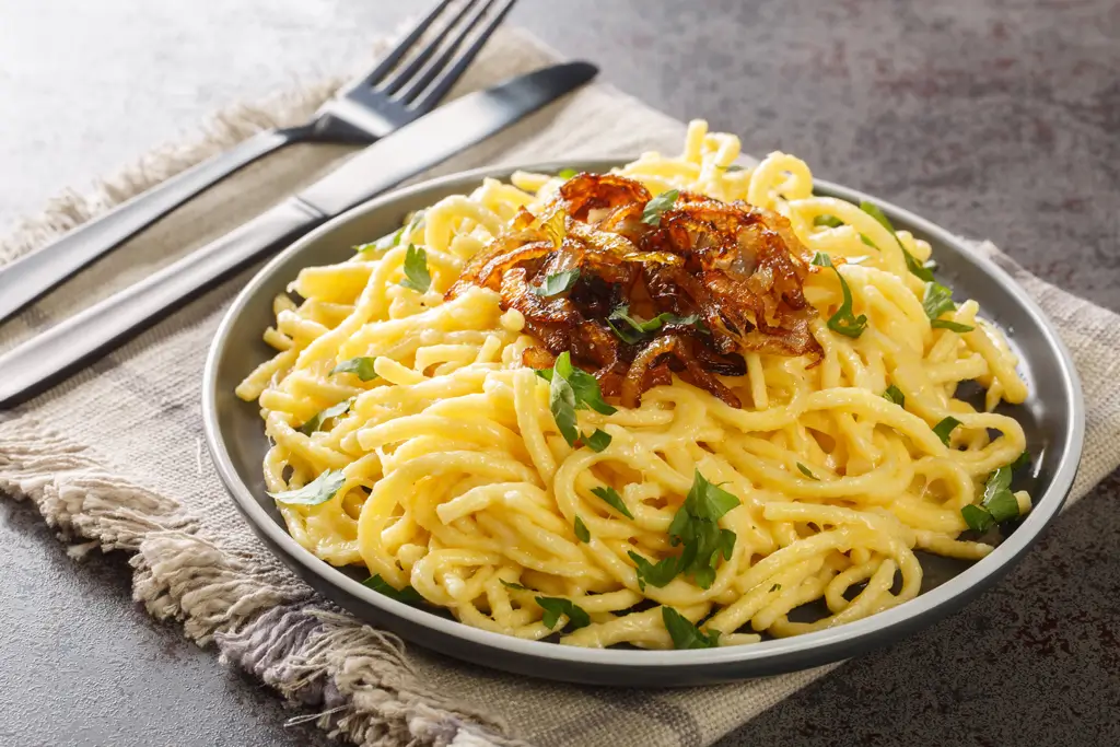 Warme Spätzlenudeln und geriebener Käse Emmentaler mit gebratenen Zwiebeln, Nahaufnahme auf dem Teller.